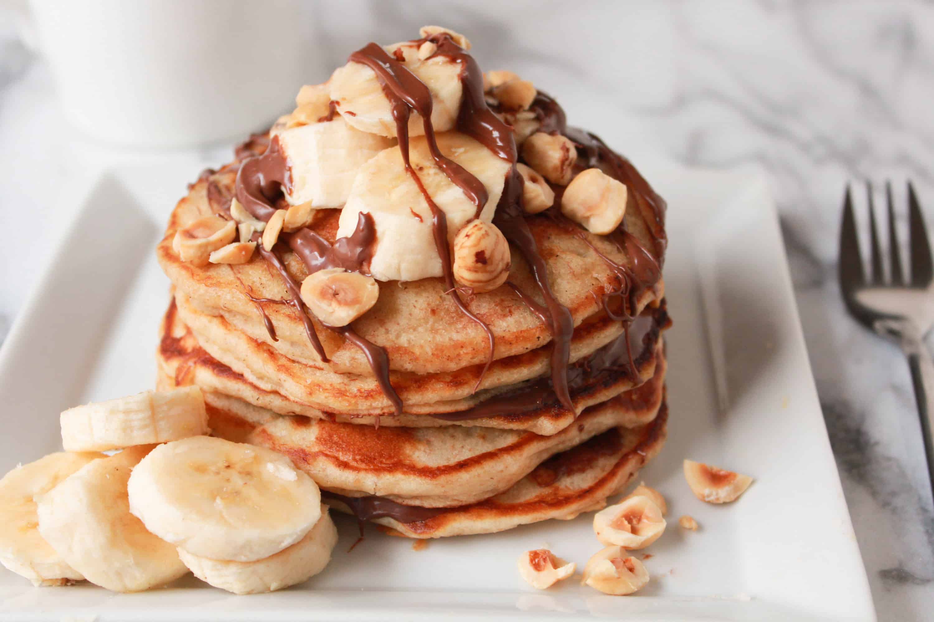 Stack of pancakes topped with banana, chocolate and nuts.