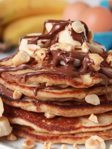 Stack of pancakes topped with banana, chocolate and nuts.