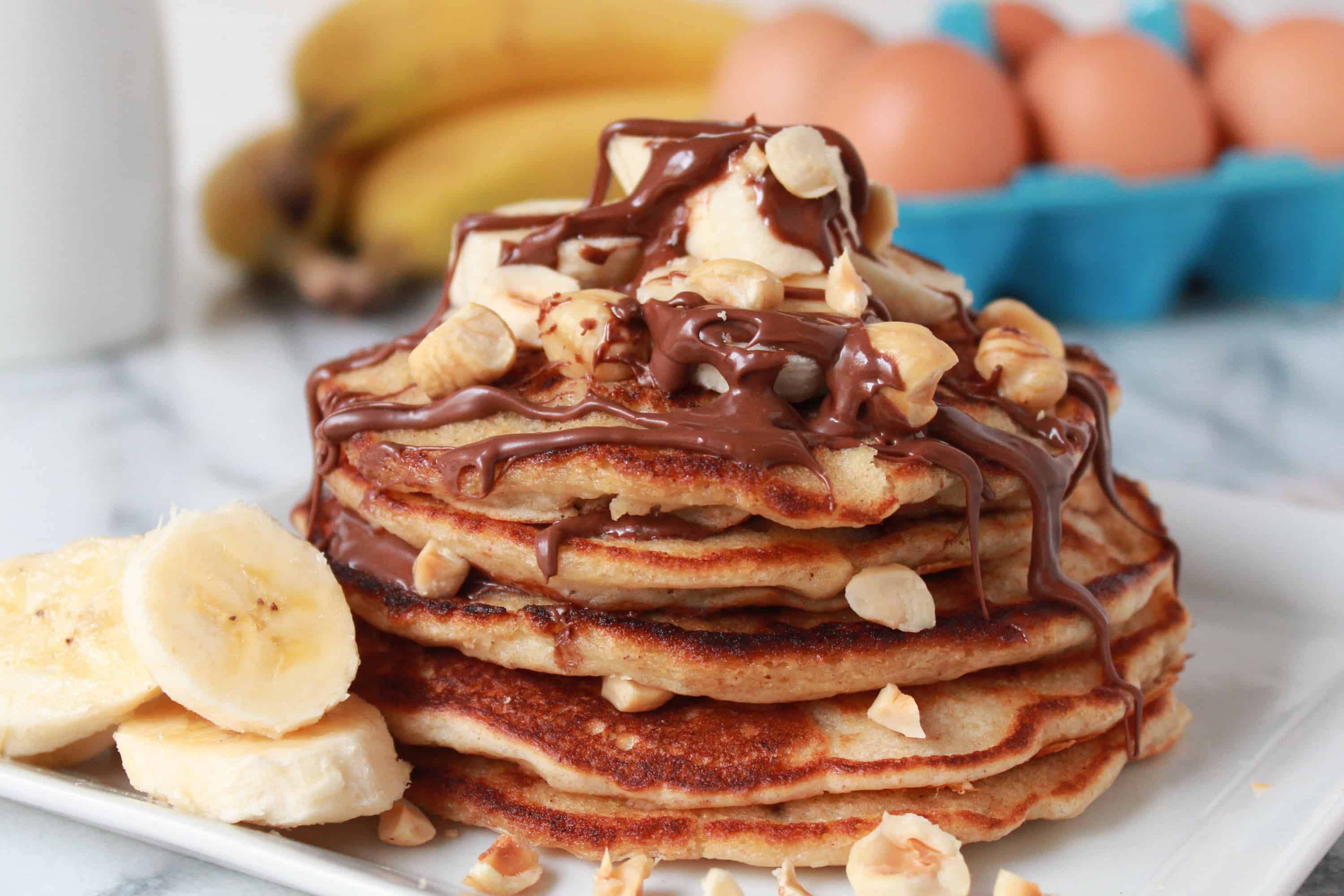 Stack of pancakes topped with banana, chocolate and nuts.