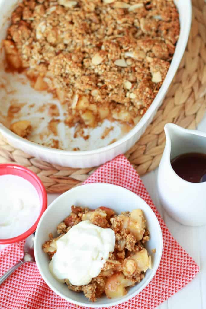 Apple crisp in a white bowl topped with yogurt.