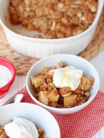 Apple crisp in a white bowl topped with yogurt.
