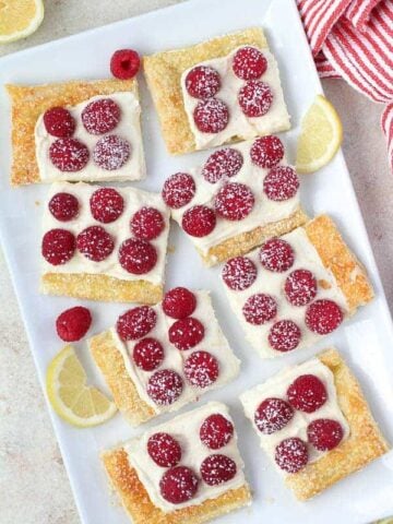 Slices of Lemon Tart topped with Raspberries on a White Platter.
