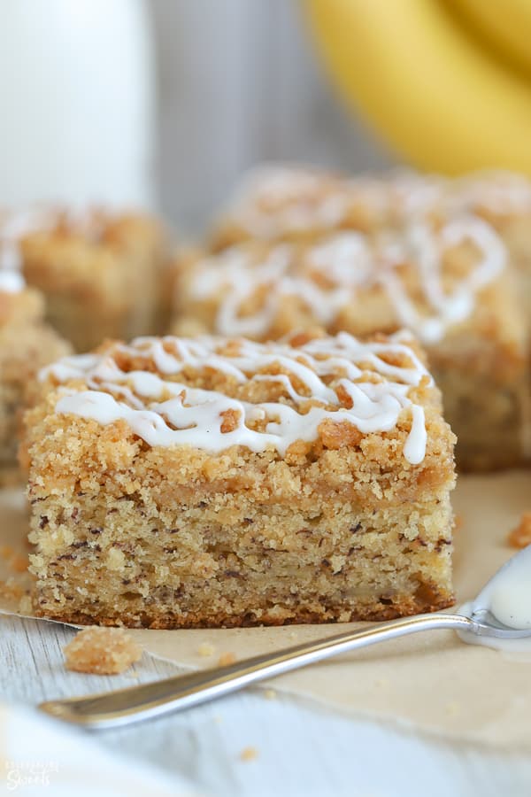 A piece of banana cake topped with white icing on a piece of parchment paper.