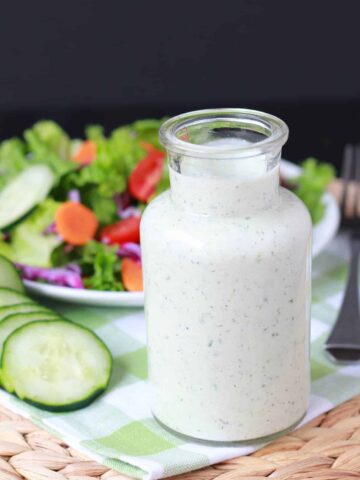 Salad dressing in a glass container with a salad in the background.