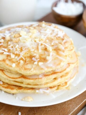 Stack of coconut pancakes topped with coconut syrup, shredded coconut and macadamia nuts.