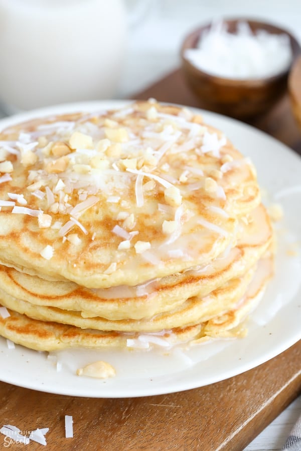 Stack of coconut pancakes topped with coconut syrup, shredded coconut and macadamia nuts.