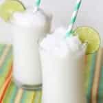 Two glasses filled with a coconut slushie garnished with lime.