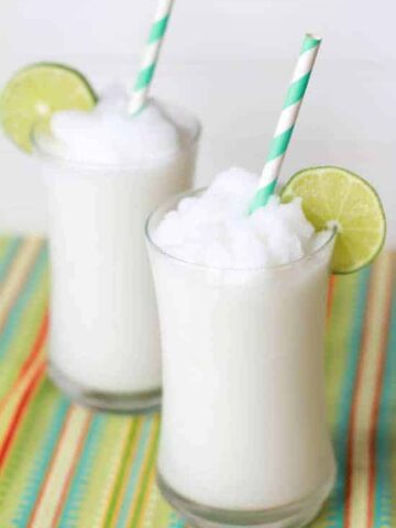 Two glasses filled with a coconut slushie garnished with lime.