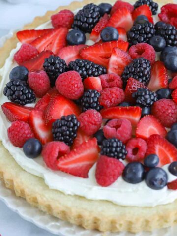Fruit tart topped with red and blue berries on a white plate.