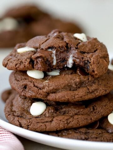 Three chocolate cookies stacked on a white plate.