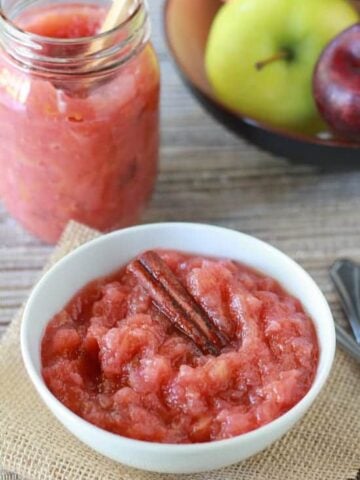 Pink applesauce in a white bowl with a cinnamon stick.