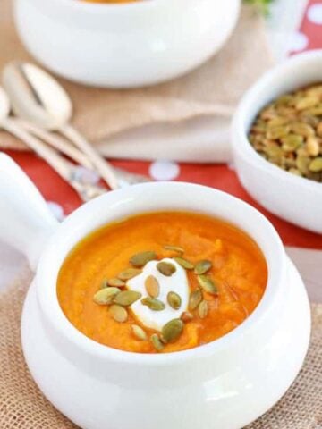Butternut squash soup in a white bowl topped with pumpkin seeds.