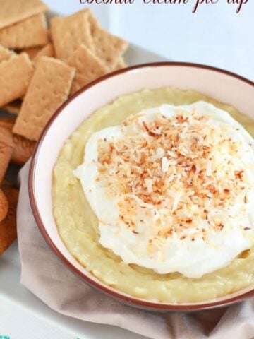 Bowl of coconut pie dip topped with whipped cream and toasted coconut.