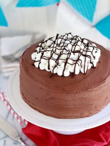 Round chocolate cake topped with marshmallows and chocolate sauce.