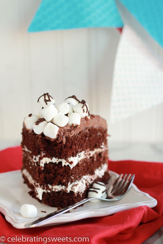 Slice of chocolate cake topped with marshmallows and chocolate sauce on a white plate.