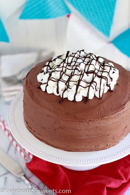 Round chocolate cake topped with marshmallows and chocolate sauce.