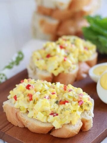 Egg salad on a piece of bread on a wooden board.