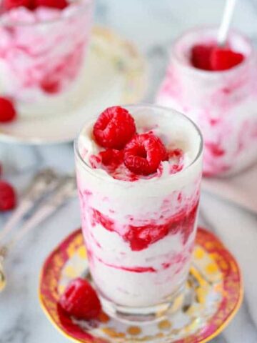 Glass filled with layers of whipped cream and raspberries.