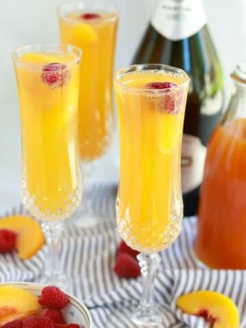 Three mimosas in champagne glasses garnished with a raspberry.