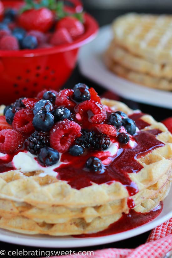 White plate with waffles, berries, and whipped cream.