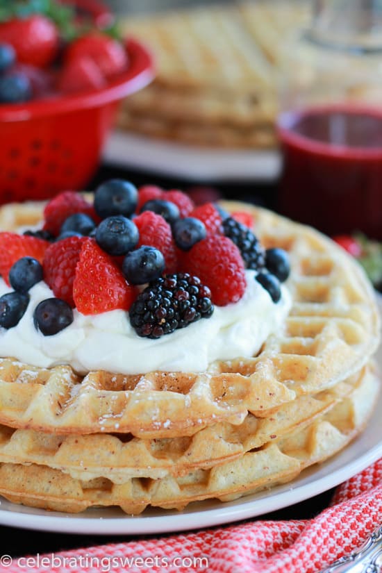 White plate with waffles, berries, and whipped cream.