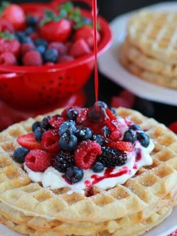 White plate with waffles, berries, and whipped cream.