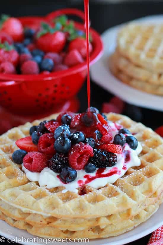 White plate with waffles, berries, and whipped cream.
