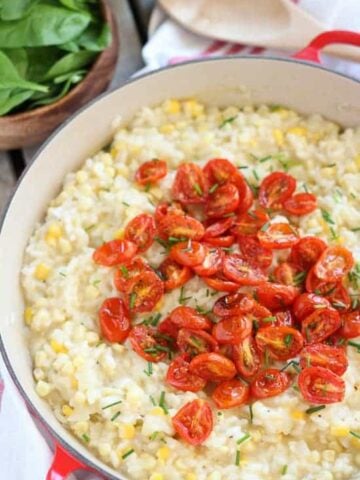 Corn risotto in a pan topped with roasted cherry tomatoes.