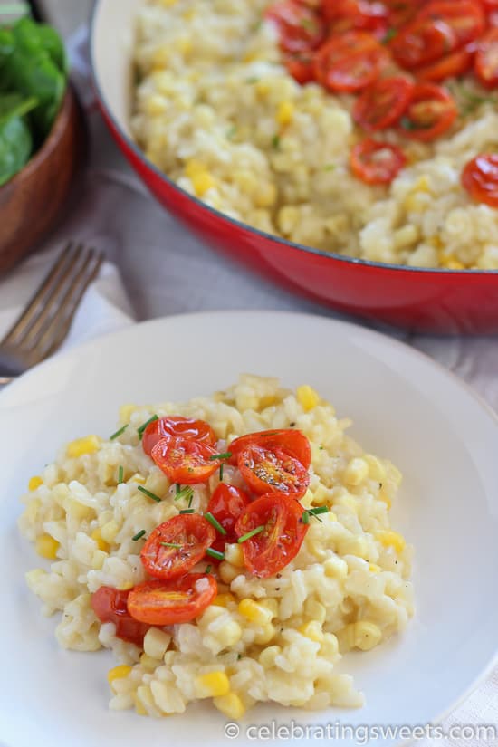 Corn risotto on a white plate topped with roasted cherry tomatoes.