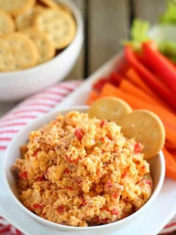White bowl filled with pimento cheese garnished with crackers and vegetables.