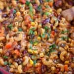 Chili mac in a skillet with a wooden spoon.