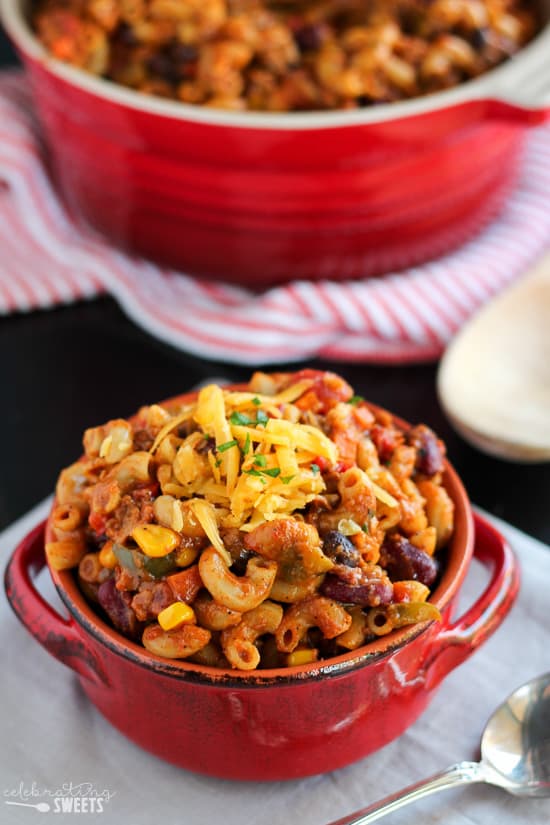 Chili mac in a red bowl topped with grated cheese.