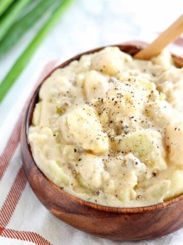 Cheesy potatoes in a wooden bowl topped with ground pepper.