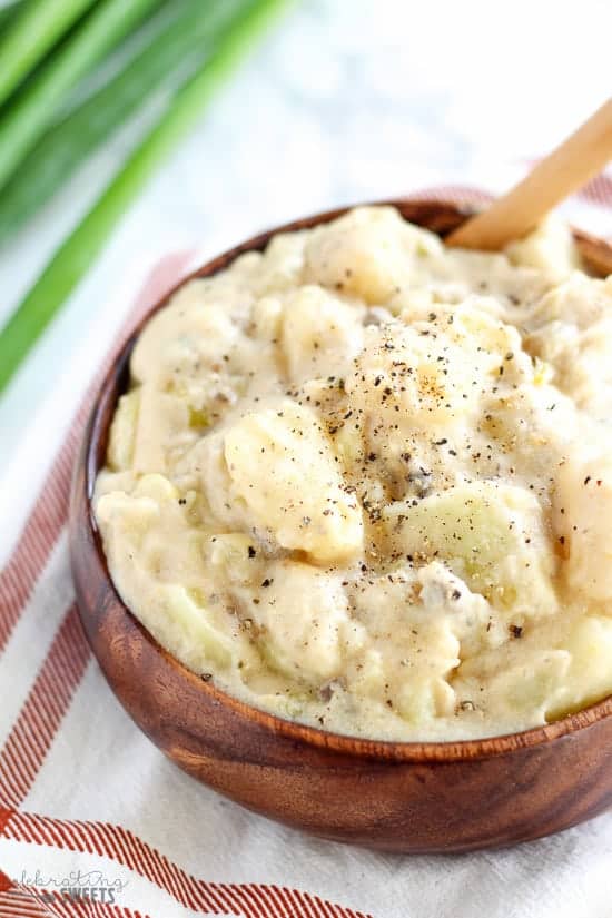 Cheesy potatoes in a wooden bowl topped with ground pepper.