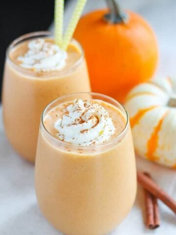 Pumpkin smoothie in a glass topped with whipped cream and cinnamon.
