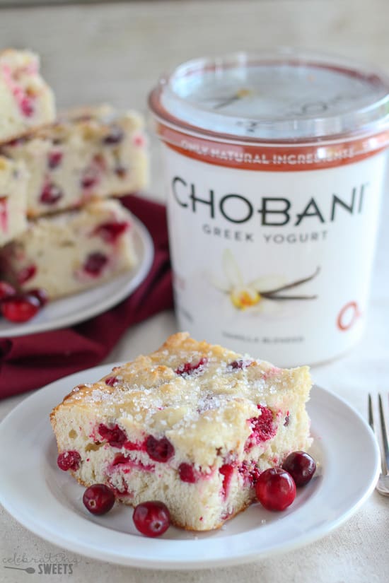 Cranberry cake on a white plate with yogurt in the background.
