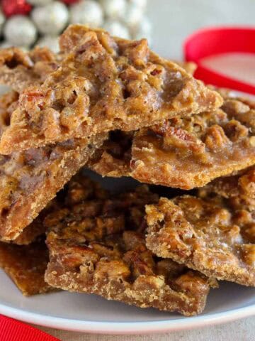 Pecan praline toffee piled on a white plate next to a red ribbon.