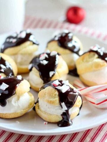 Cream puffs covered in chocolate on a white plate.