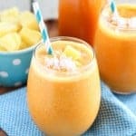 Carrot smoothie in a glass with a turquoise napkin underneath.