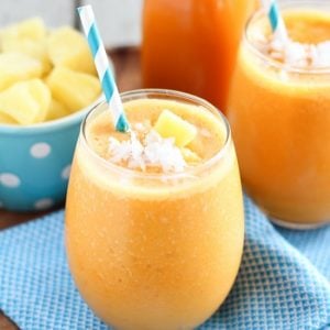 Carrot smoothie in a glass with a turquoise napkin underneath.