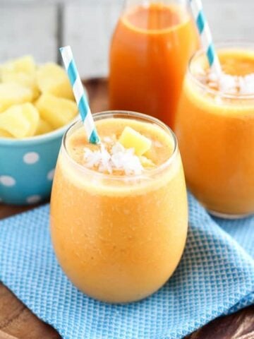 Carrot smoothie in a glass with a turquoise napkin underneath.