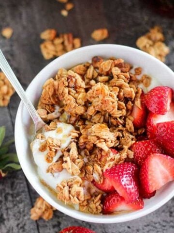 White bowl with granola, yogurt and strawberries.