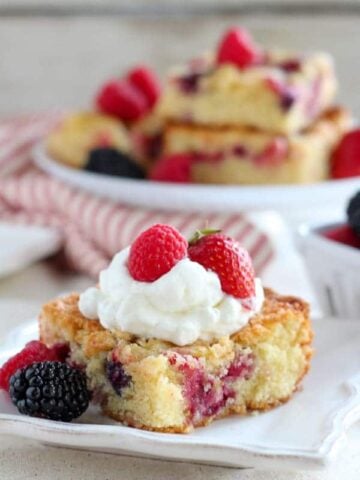 Close up of a slice of berry cake topped with whipped cream and berries.