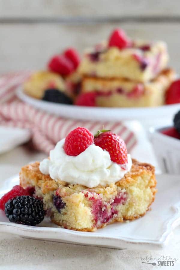 Close up of a slice of berry cake topped with whipped cream and berries.