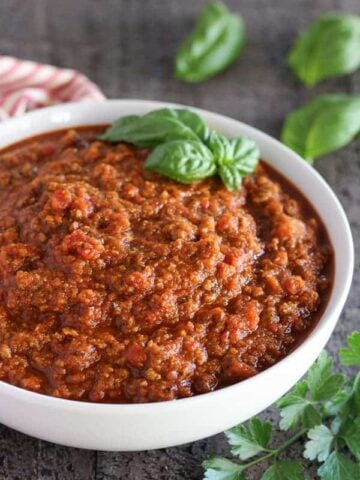 Meat sauce in a white bowl garnished with basil.