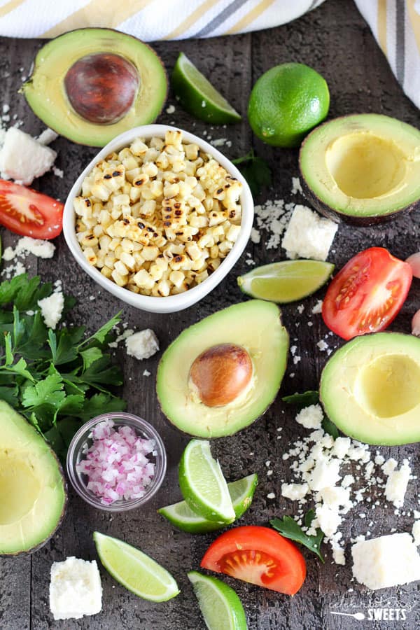 Avocado, corn, tomato, cheese, and lime on a dark board.