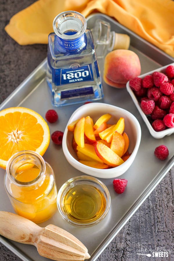 Peaches, raspberries, tequila, and orange juice on a metal tray.