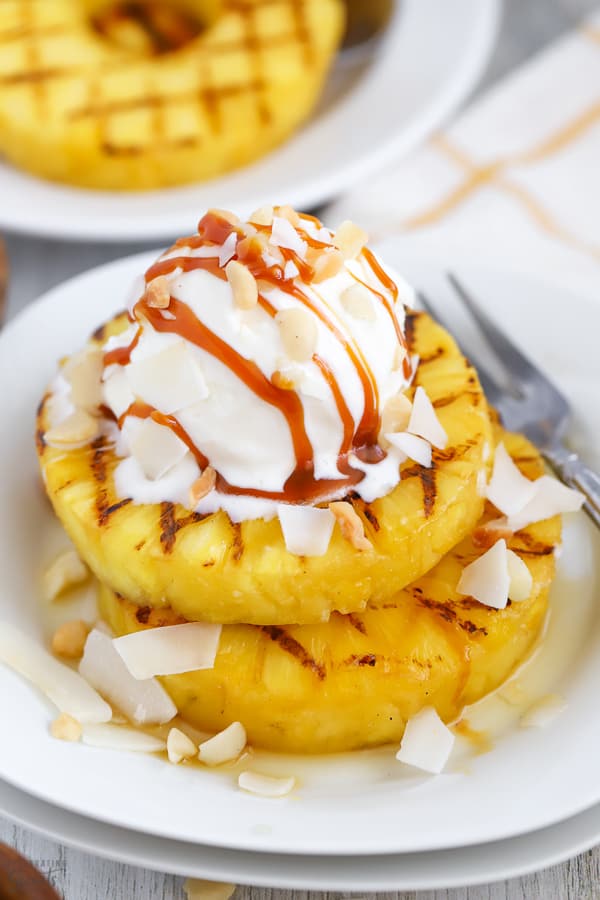 Grilled pineapple on a white plate topped with ice cream.