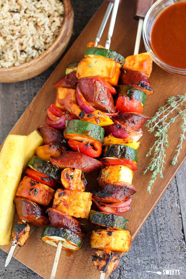 Skewers with grilled sausage and vegetables on a wooden board.