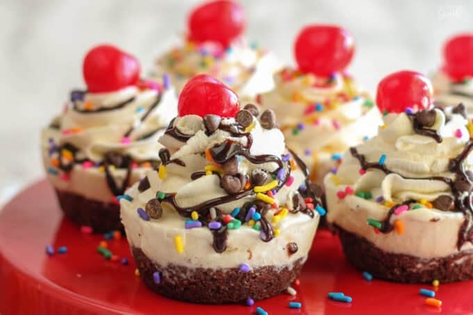 Ice cream cupcakes on a red plate topped with sundae toppings.